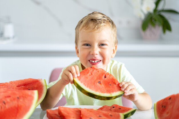 Enfant Dans La Cuisine De La Maison Un Bebe Mange Une Pasteque Sourit Le Concept D Une Alimentation Saine Photo Premium Enfant Dans La Cuisine De La Maison Un Bebe Mange Une Pasteque Sourit Le Concept D Une Alimentation Saine Photo Premium