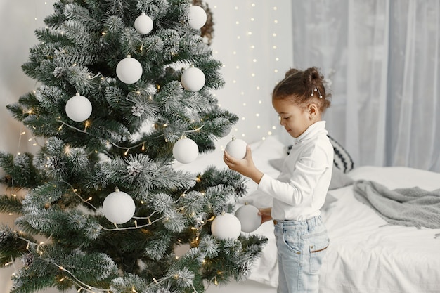 Enfant dans un pull blanc. Fille debout près de l'arbre de Noël.