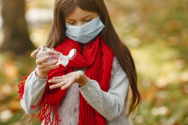 Enfant Debout Dans Le Parc De L'automne. Thème Du Coronavirus. Fille Dans Un Foulard Rouge. Les Enfants Utilisent Un Antiseptique.