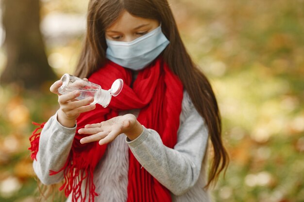 Enfant debout dans le parc de l'automne. Thème du coronavirus. Fille dans un foulard rouge. Les enfants utilisent un antiseptique.