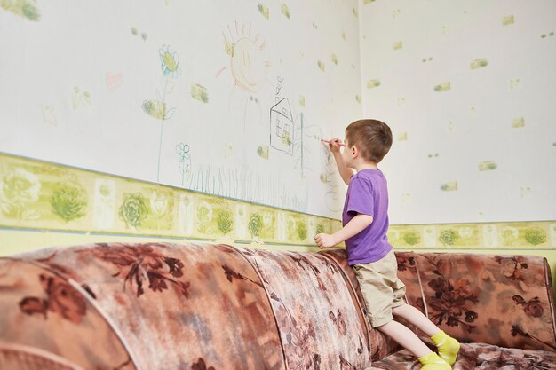 L'enfant dessine sur le papier peint debout sur le canapé du salon. le concept d'auto-isolement pendant le coronavirus.