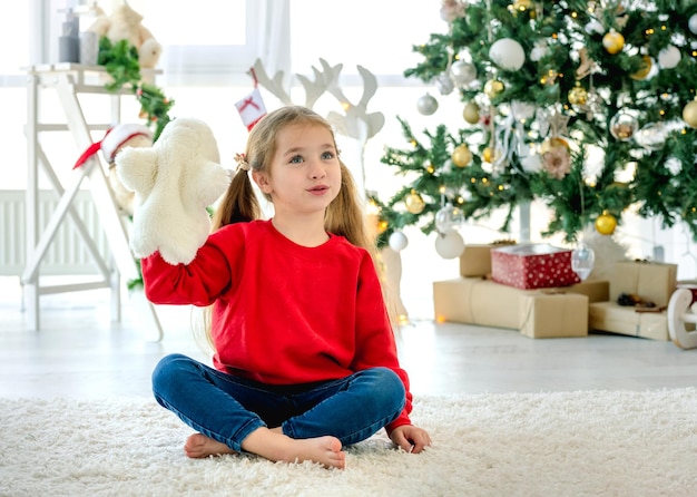 Enfant fille à noël assis sur un tapis dans la chambre avec arbre décoré et cadeaux. joli enfant à la maison pendant les vacances du nouvel an