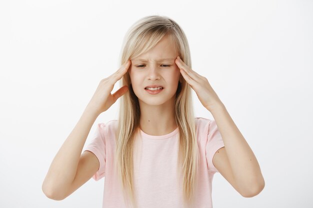 L'enfant inquiet non focalisé ne peut pas penser clairement et garder l'information à l'esprit. Inquiète jeune fille confuse aux cheveux blonds, tenant les mains sur les tempes et grimaçant, essayant de se souvenir de quelque chose