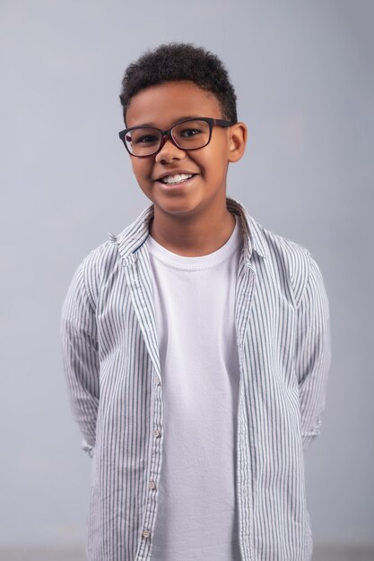 Enfant joyeux dans des lunettes élégantes debout sur le fond blanc