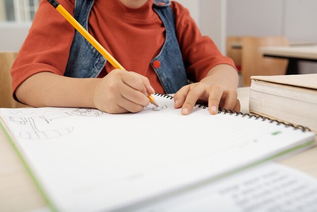 Enfant méconnaissable assis au bureau et dessinant dans un cahier avec un crayon