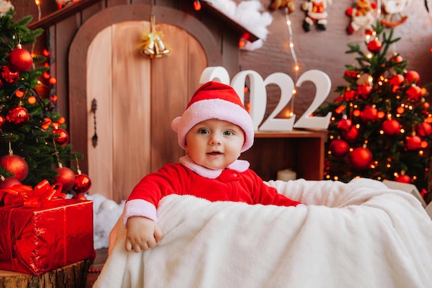 Un enfant mignon déguisé en père noël est assis près de l'arbre de noël. marchandises pour les enfants et les vacances. concept de nouvel an d'hiver. noël 2022