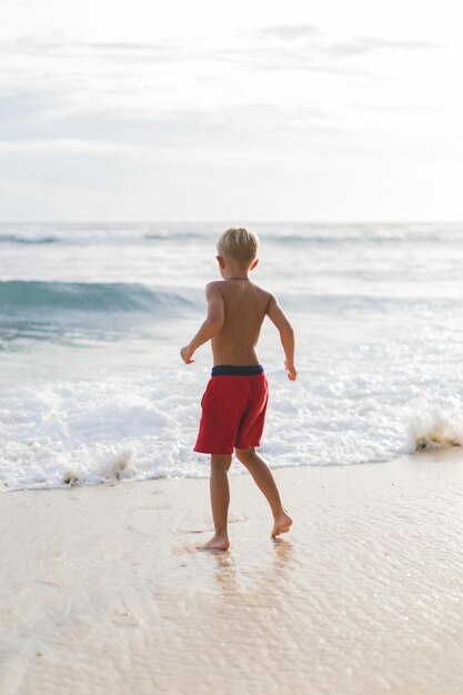 Un enfant sur la plage joue dans les vagues de l'océan. Garçon sur l'océan, enfance heureuse. vie tropicale.