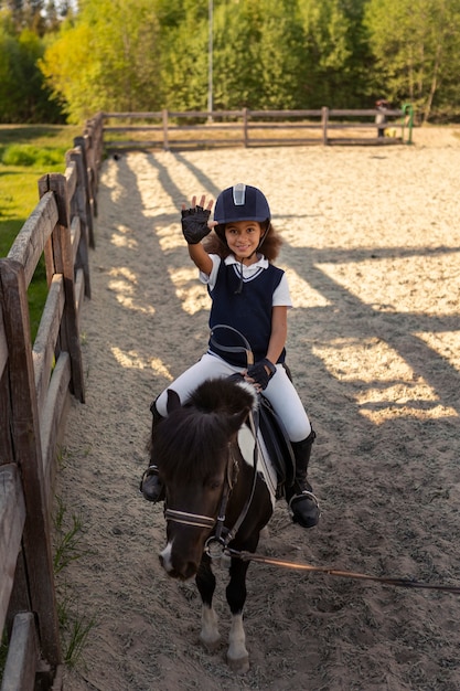 Photo gratuite enfant plein coup apprenant à monter à cheval