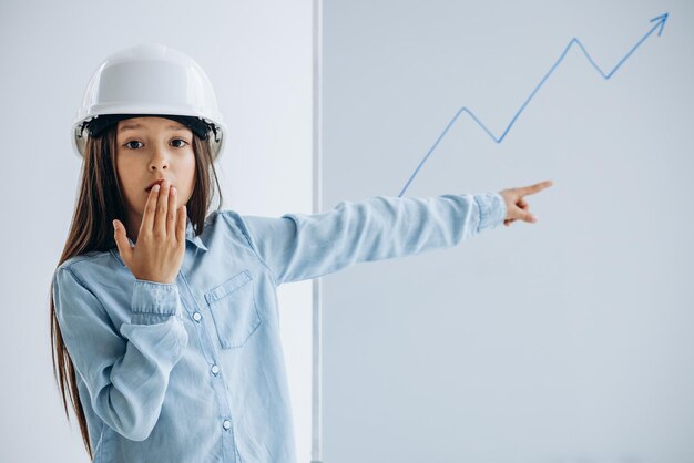 Enfant portant un chapeau de sécurité blanc debout près du tableau blanc dessinant une flèche d'analyse