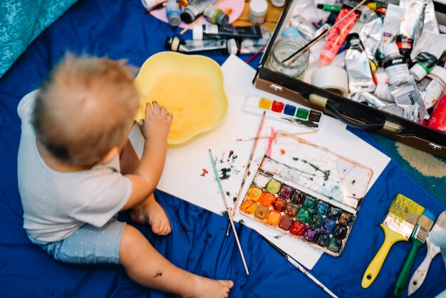 Enfant près de pinceaux, aquarelles et boîte assise sur la couverture