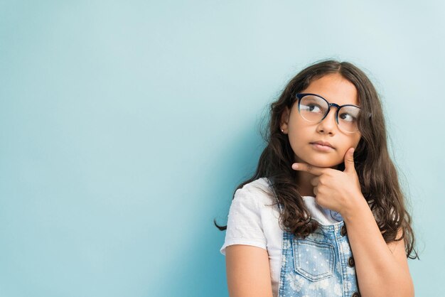 Enfant de sexe féminin réfléchi avec la main sur le menton regardant loin sur fond turquoise