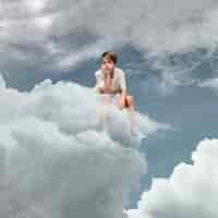 Photo gratuite enfant triste plein coup assis sur un nuage