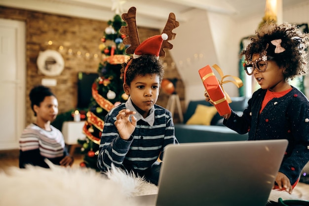 Enfants afro-américains faisant un appel vidéo sur un ordinateur portable à Noël à la maison