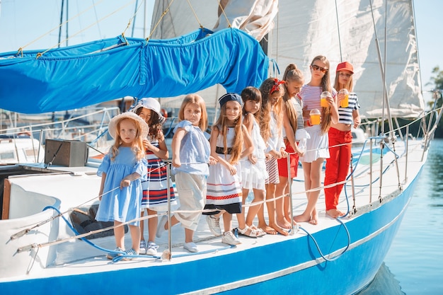 Photo gratuite les enfants à bord du yacht de mer buvant du jus d'orange. les filles adolescentes ou enfants contre le ciel bleu en plein air. des vêtements colorés. mode enfantine, été ensoleillé, rivière et concepts de vacances.