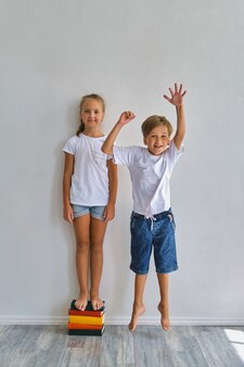Enfants cool, petit garçon et fille mesurent leur taille et comparent, s'amusent près du mur blanc