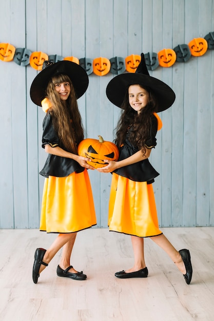 Photo gratuite enfants en costumes de sorcière posant et tenant la citrouille d'halloween