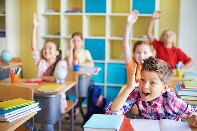 Photo gratuite les enfants dans la salle de classe avec leurs mains vers le haut