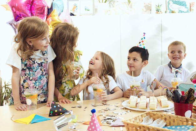 enfants et décorations d'anniversaire. garçons et filles à table avec de la nourriture, des gâteaux, des boissons et des gadgets de fête.