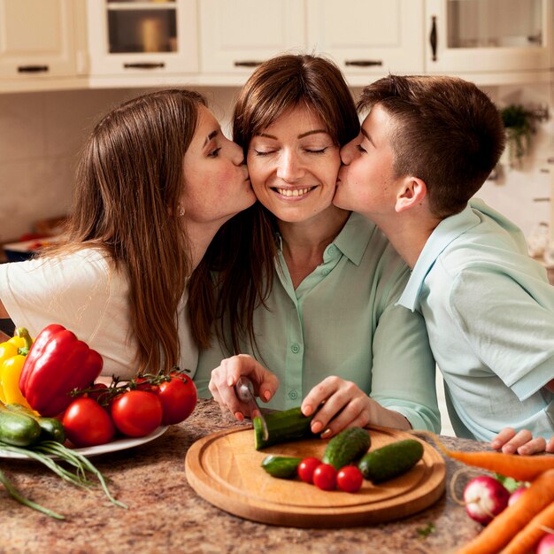 Enfants donnant un baiser à la mère dans la cuisine tout en préparant la nourriture