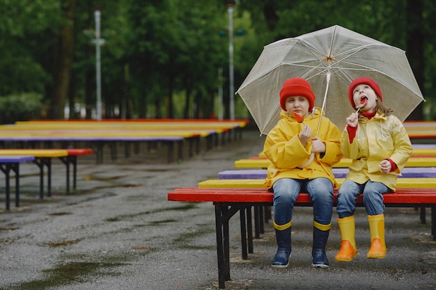 Enfants drôles en bottes de pluie jouant dans un parc pluvieux