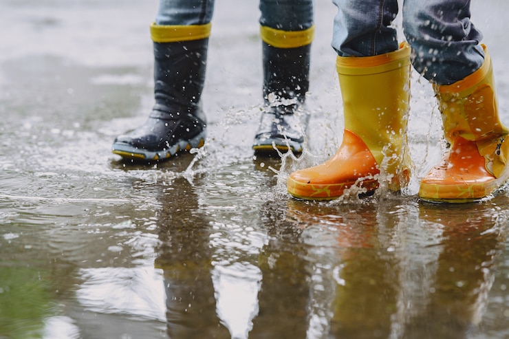 Photo gratuit enfants drôles en bottes de pluie jouant avec un navire en papier par une flaque d'eau