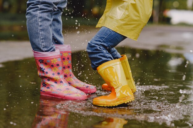 Enfants drôles en bottes de pluie jouant avec un navire en papier par une flaque d'eau