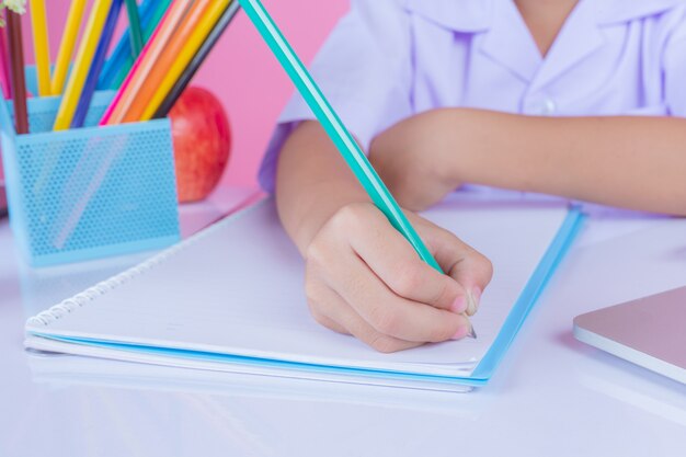 Les enfants écrivent des gestes de livre sur un fond rose.