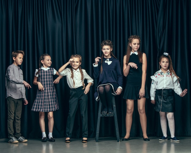 Enfants élégants mignons sur un espace sombre. Les belles adolescentes et garçon debout ensemble