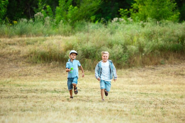 Enfants, enfants qui courent sur le pré au soleil d'été. Ayez l'air heureux, joyeux avec des émotions lumineuses sincères. Garçons et filles caucasiens mignons.