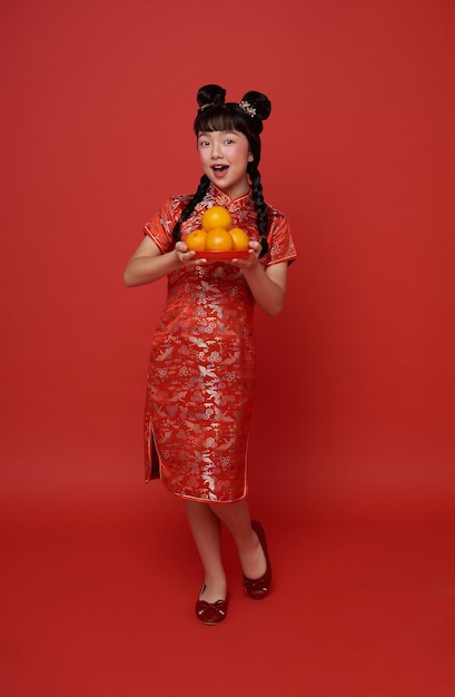 Photo gratuite enfants fille asiatique en costume traditionnel rouge donnant des oranges fraîches pour bénir le nouvel an chinois