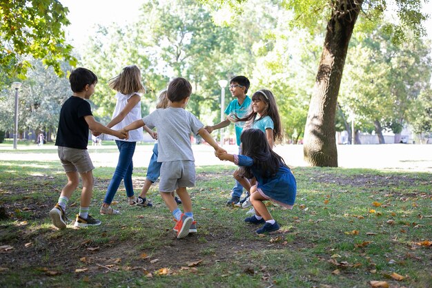 Des enfants heureux jouent ensemble à l'extérieur, dansent sur l'herbe, profitent d'activités de plein air et s'amusent dans le parc. Concept de fête ou d'amitié pour enfants