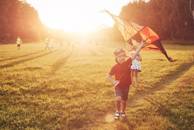 Des enfants heureux lancent un cerf-volant sur le terrain au coucher du soleil. Petit garçon et fille en vacances d'été