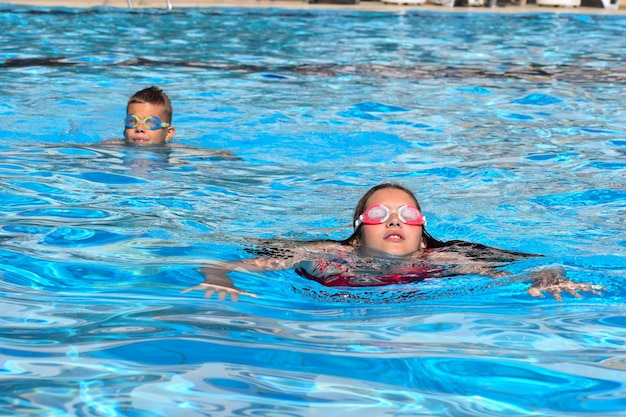 Les enfants nagent dans la piscine à l'extérieur du parc aquatique. enfants joyeux sports nautiques actifs en été. vacances d'enfants à la mer