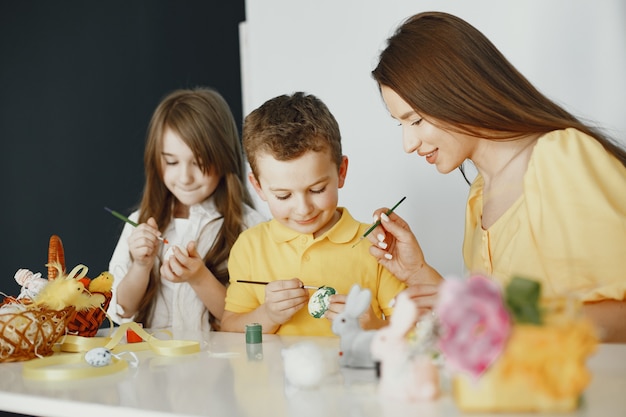 Les enfants peignent des œufs. Mère enseigne aux enfants. Assis à une table blanche.