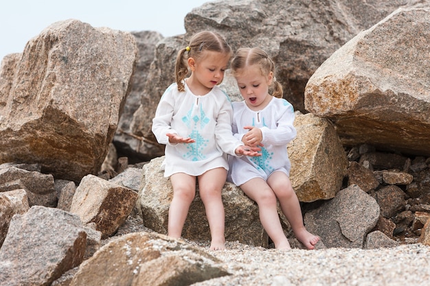 Enfants sur la plage de la mer. Jumeaux assis contre des pierres et de l'eau de mer.