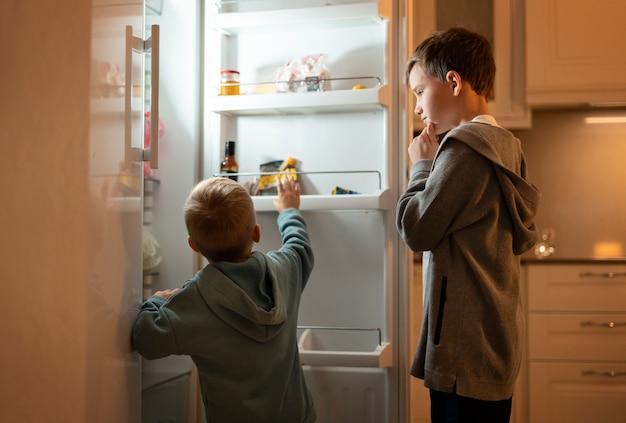 Enfants de plan moyen regardant dans le réfrigérateur