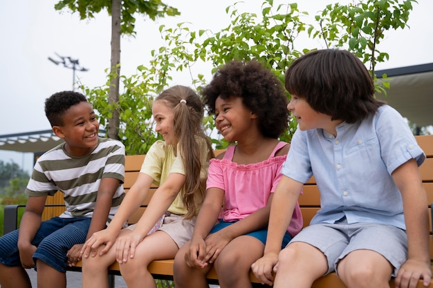 Enfants souriants de plan moyen assis sur un banc