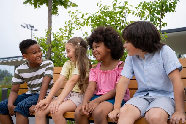 Enfants souriants de plan moyen assis sur un banc