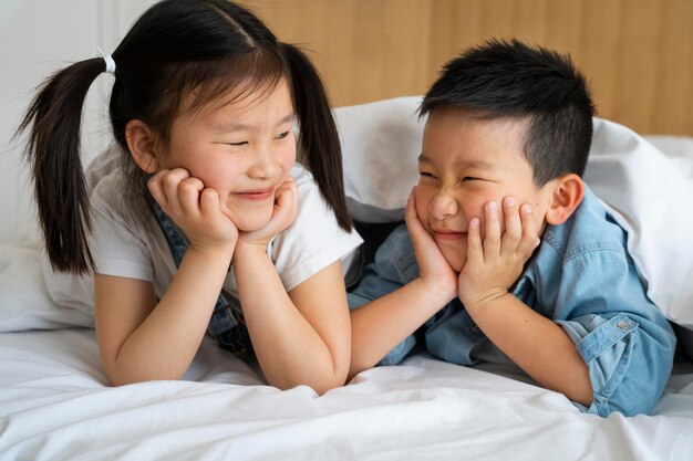 Enfants souriants de plan moyen au lit