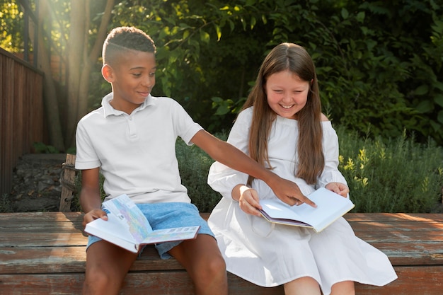 Enfants souriants à plan moyen lisant à l'extérieur