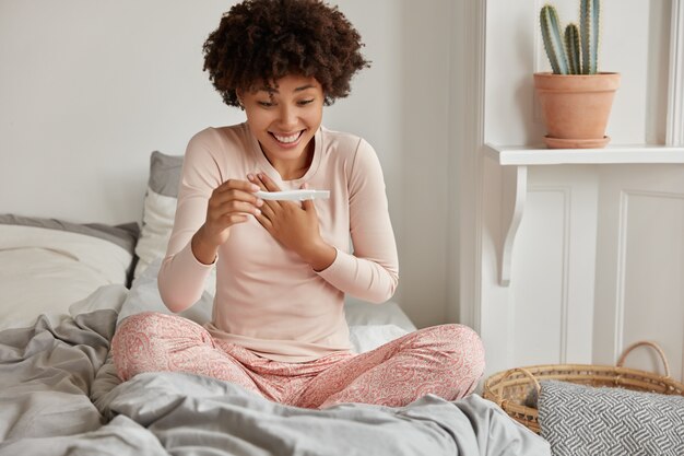 Enfin enceinte. Heureuse femme afro-américaine ne peut pas croire au résultat du test de grossesse positif, semble positivement