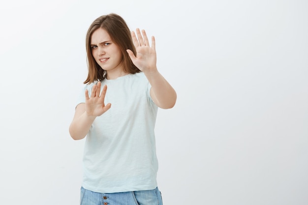 Enlevez-moi ça. Portrait de femme européenne mignonne mécontent et irrité intense en t-shirt à la mode couvrant le visage avec les bras tirés se détournant avec un regard mécontent d'être aveuglé par une lampe de poche