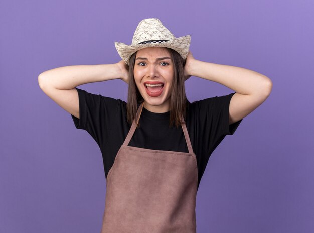 Ennuyé assez caucasien femme jardinier portant chapeau de jardinage fermant les oreilles avec les mains sur le violet