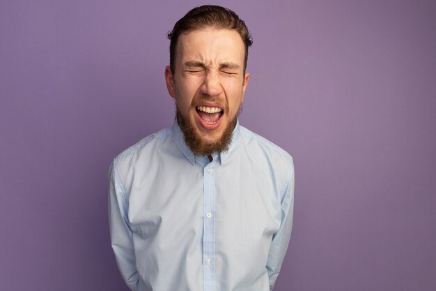 Ennuyé bel homme blond hurle les yeux fermés isolés sur le mur violet