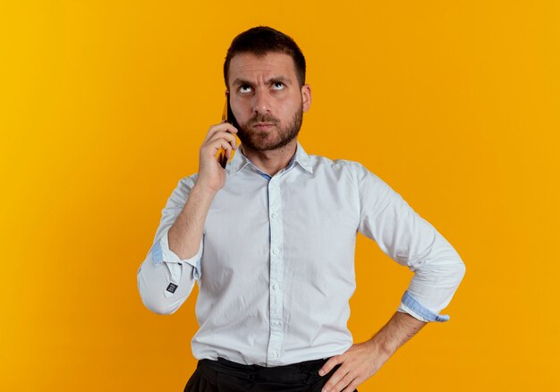 Ennuyé bel homme parle au téléphone à la recherche d'isolement sur le mur orange