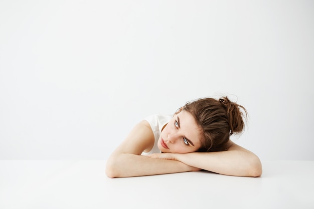 Ennuyé fatigué jeune jolie femme avec chignon pensant rêver allongé sur la table sur fond blanc.