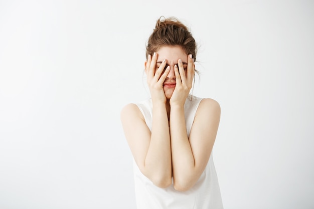 Ennuyé fatigué jeune jolie femme se cachant le visage derrière les mains.