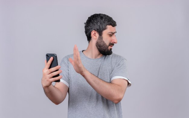 Ennuyé jeune bel homme caucasien regardant côté tenant le téléphone mobile et faisant des gestes pas isolé sur blanc avec espace de copie