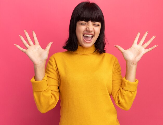 Ennuyé jeune fille caucasienne brune se tient avec les mains levées sur rose