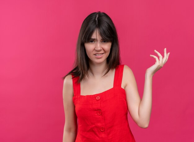 Ennuyé jeune fille caucasienne tenant la main vide regardant la caméra sur fond rose isolé avec copie espace